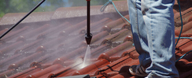 Man pressure washing a red shingled rooftop