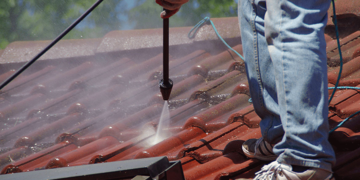 Man pressure washing a red shingled rooftop