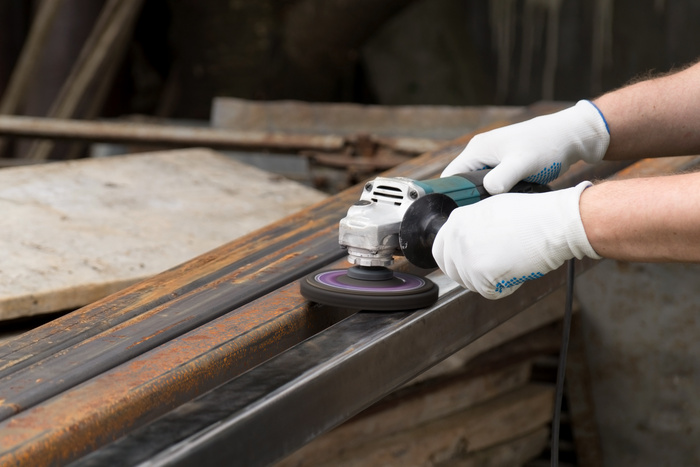 A man working with electric angle grinder tool. Removing rust a metal square tube.